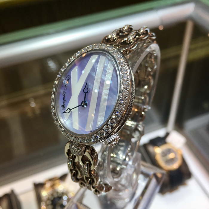 Breguet 宝玑 Reine de Naples 那不勒斯皇后系列 ，9818BB/5V/J51 DDD0。32.7x27.3毫米表径，18K白金镶钻表壳，鹅卵形表壳，表壳外缘饰有钱币纹。表圈和表耳上镶嵌64颗明亮式切割钻石（约1.654克拉），表冠处镶有一颗梨形钻石（约0.15克拉）。淡紫色珍珠贝母面，镌刻独立编号和Breguet隐形签名。6点位置设有偏心小时刻度环，采用罗马数字时标，镶刻白色天然珍珠母贝雕饰。宝玑经典针尖镂空式蓝钢指针。自动上弦机械机芯，动力储备38小时。 全套附件齐全。