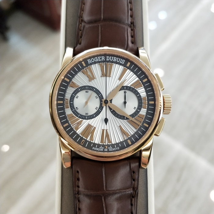 RogerDubuis 罗杰杜彼 Hommage 致敬系列，RDDBHO0569。42毫米表径。18K玫瑰金表壳， 手工玑镂饰纹表盘，腕表采用造型大胆的长方形按把和布满凹槽线条的表冠，展现出鲜明的阳刚性格，却又以优美的圆弧曲线以及长秒针的叶形尾端带来柔和的色彩。位于3点钟和9点钟位置的蜗形纹计时圈有力地见证着传统制表同样能够符合现代精确计时需求的事实。蓝宝石水晶玻璃表镜。RD680 自动上弦机械机芯，搭载微型摆陀。动力储备52小时。 全套附件齐全。