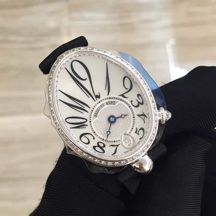 Breguet 宝玑 Reine de Naples 那不勒斯皇后系列，8918BB/58/864/D00D。18K白金鹅卵形表壳，36.5 x 28.45毫米表径。表壳外缘饰有钱币纹。表圈和表壳周围镶嵌117颗明亮式切割钻石（约0.99克拉）。表冠处镶有一颗梨形钻石（约0.26克拉）。蓝宝石水晶底盖。表盘为大溪地天然白色珍珠母贝，采用玑镂刻花处理。具有独立编号与Breguet隐形签名。偏心刻度环位于6点位置，采用宝玑阿拉伯数字时符。6点位镶嵌梨形钻石（约0.09克拉）。经典的蓝钢宝玑指针。金质折叠表扣，镶嵌26颗明亮式切割钻石（约0.12克拉）。537/3自动上链机芯，动力储备45小时。