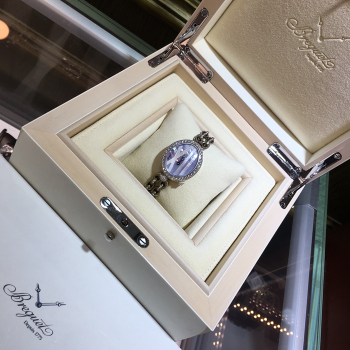 Breguet 宝玑 Reine de Naples 那不勒斯皇后系列 ，9818BB/5V/J51 DDD0。32.7x27.3毫米表径，18K白金镶钻表壳，鹅卵形表壳，表壳外缘饰有钱币纹。表圈和表耳上镶嵌64颗明亮式切割钻石（约1.654克拉），表冠处镶有一颗梨形钻石（约0.15克拉）。淡紫色珍珠贝母面，镌刻独立编号和Breguet隐形签名。6点位置设有偏心小时刻度环，采用罗马数字时标，镶刻白色天然珍珠母贝雕饰。宝玑经典针尖镂空式蓝钢指针。自动上弦机械机芯，动力储备38小时。 全套附件齐全。