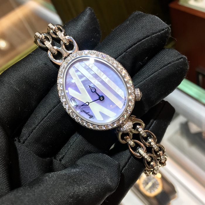 Breguet 宝玑 Reine de Naples 那不勒斯皇后系列 ，9818BB/5V/J51 DDD0。32.7x27.3毫米表径，18K白金镶钻表壳，鹅卵形表壳，表壳外缘饰有钱币纹。表圈和表耳上镶嵌64颗明亮式切割钻石（约1.654克拉），表冠处镶有一颗梨形钻石（约0.15克拉）。淡紫色珍珠贝母面，镌刻独立编号和Breguet隐形签名。6点位置设有偏心小时刻度环，采用罗马数字时标，镶刻白色天然珍珠母贝雕饰。宝玑经典针尖镂空式蓝钢指针。自动上弦机械机芯，动力储备38小时。 全套附件齐全。
