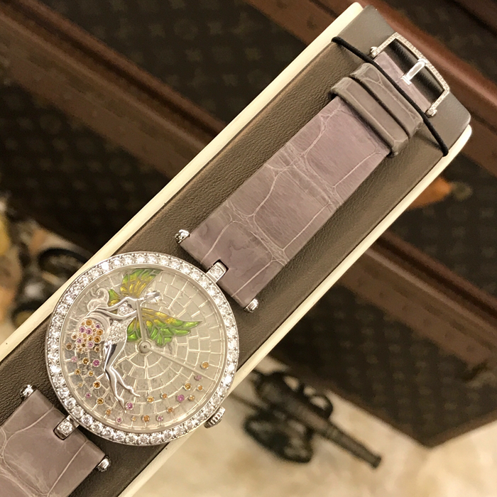  梵克雅宝非凡表盘腕表系列，花仙子，VCARO30900。18K白金表壳钻圈，38毫米表径。表盘微型马赛克珐琅，饰有银箔。雕刻18K白金躯体的女神，身穿饰满圆形钻石的裙子。白金脸孔镶嵌玫瑰形切割钻石。彩绘玻璃珐琅白金翅膀，雕刻白金号角，镶嵌圆形粉红色蓝宝石和锰铝榴石。手动上弦机械机芯，动力储备约60小时。专柜定价：880000元。