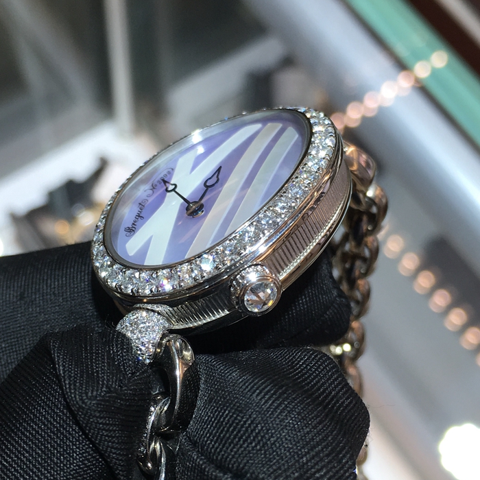 Breguet 宝玑 Reine de Naples 那不勒斯皇后系列 ，9818BB/5V/J51 DDD0。32.7x27.3毫米表径，18K白金镶钻表壳，鹅卵形表壳，表壳外缘饰有钱币纹。表圈和表耳上镶嵌64颗明亮式切割钻石（约1.654克拉），表冠处镶有一颗梨形钻石（约0.15克拉）。淡紫色珍珠贝母面，镌刻独立编号和Breguet隐形签名。6点位置设有偏心小时刻度环，采用罗马数字时标，镶刻白色天然珍珠母贝雕饰。宝玑经典针尖镂空式蓝钢指针。自动上弦机械机芯，动力储备38小时。 全套附件齐全。