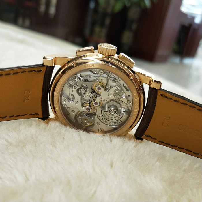 RogerDubuis 罗杰杜彼 Hommage 致敬系列，RDDBHO0569。42毫米表径。18K玫瑰金表壳， 手工玑镂饰纹表盘，腕表采用造型大胆的长方形按把和布满凹槽线条的表冠，展现出鲜明的阳刚性格，却又以优美的圆弧曲线以及长秒针的叶形尾端带来柔和的色彩。位于3点钟和9点钟位置的蜗形纹计时圈有力地见证着传统制表同样能够符合现代精确计时需求的事实。蓝宝石水晶玻璃表镜。RD680 自动上弦机械机芯，搭载微型摆陀。动力储备52小时。 全套附件齐全。