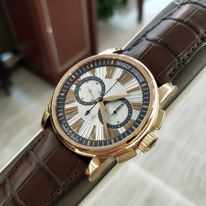 RogerDubuis 罗杰杜彼 Hommage 致敬系列，RDDBHO0569。42毫米表径。18K玫瑰金表壳， 手工玑镂饰纹表盘，腕表采用造型大胆的长方形按把和布满凹槽线条的表冠，展现出鲜明的阳刚性格，却又以优美的圆弧曲线以及长秒针的叶形尾端带来柔和的色彩。位于3点钟和9点钟位置的蜗形纹计时圈有力地见证着传统制表同样能够符合现代精确计时需求的事实。蓝宝石水晶玻璃表镜。RD680 自动上弦机械机芯，搭载微型摆陀。动力储备52小时。 全套附件齐全。