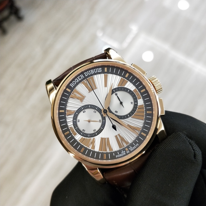 RogerDubuis 罗杰杜彼 Hommage 致敬系列，RDDBHO0569。42毫米表径。18K玫瑰金表壳， 手工玑镂饰纹表盘，腕表采用造型大胆的长方形按把和布满凹槽线条的表冠，展现出鲜明的阳刚性格，却又以优美的圆弧曲线以及长秒针的叶形尾端带来柔和的色彩。位于3点钟和9点钟位置的蜗形纹计时圈有力地见证着传统制表同样能够符合现代精确计时需求的事实。蓝宝石水晶玻璃表镜。RD680 自动上弦机械机芯，搭载微型摆陀。动力储备52小时。 全套附件齐全。