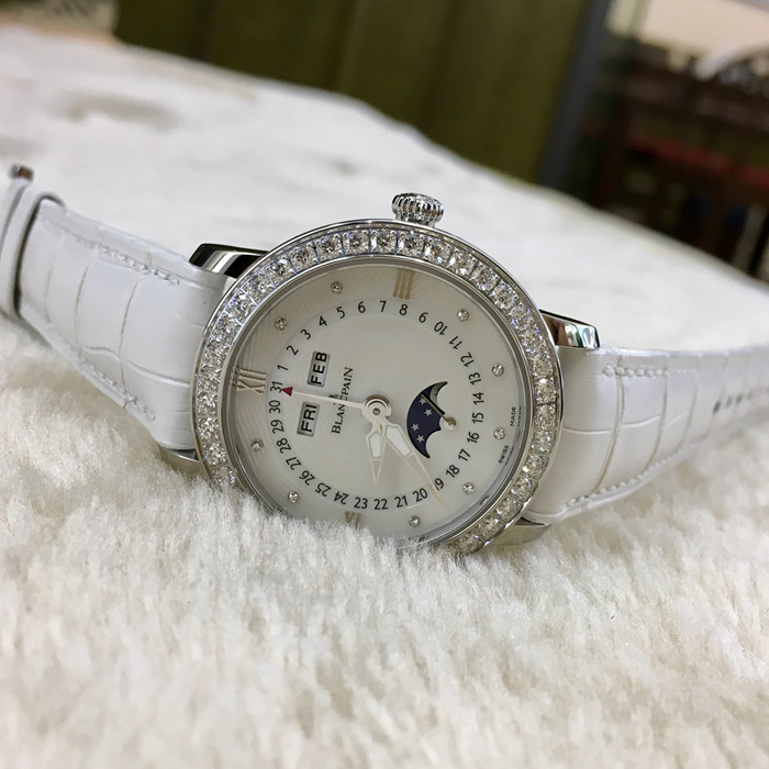 Blancpain 宝珀 WOMEN 女装系列，3663A-4654-55B。35毫米表径，精钢材质，透明表底，表圈镶嵌40壳明亮式钻石，约1.95克拉。珍珠贝母面镶嵌美钻，中心指针式日期显示，视窗式月份、星期、月相显示，六时位小秒针。自产 Cal.6763 自动上弦机械机芯，动力储备100小时。专柜定价148500元。 未使用品全套附件齐全。